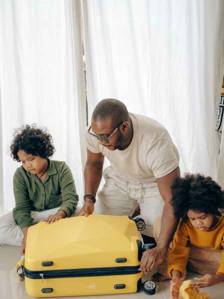 A man of color helps two sons pack a yellow suitcase.