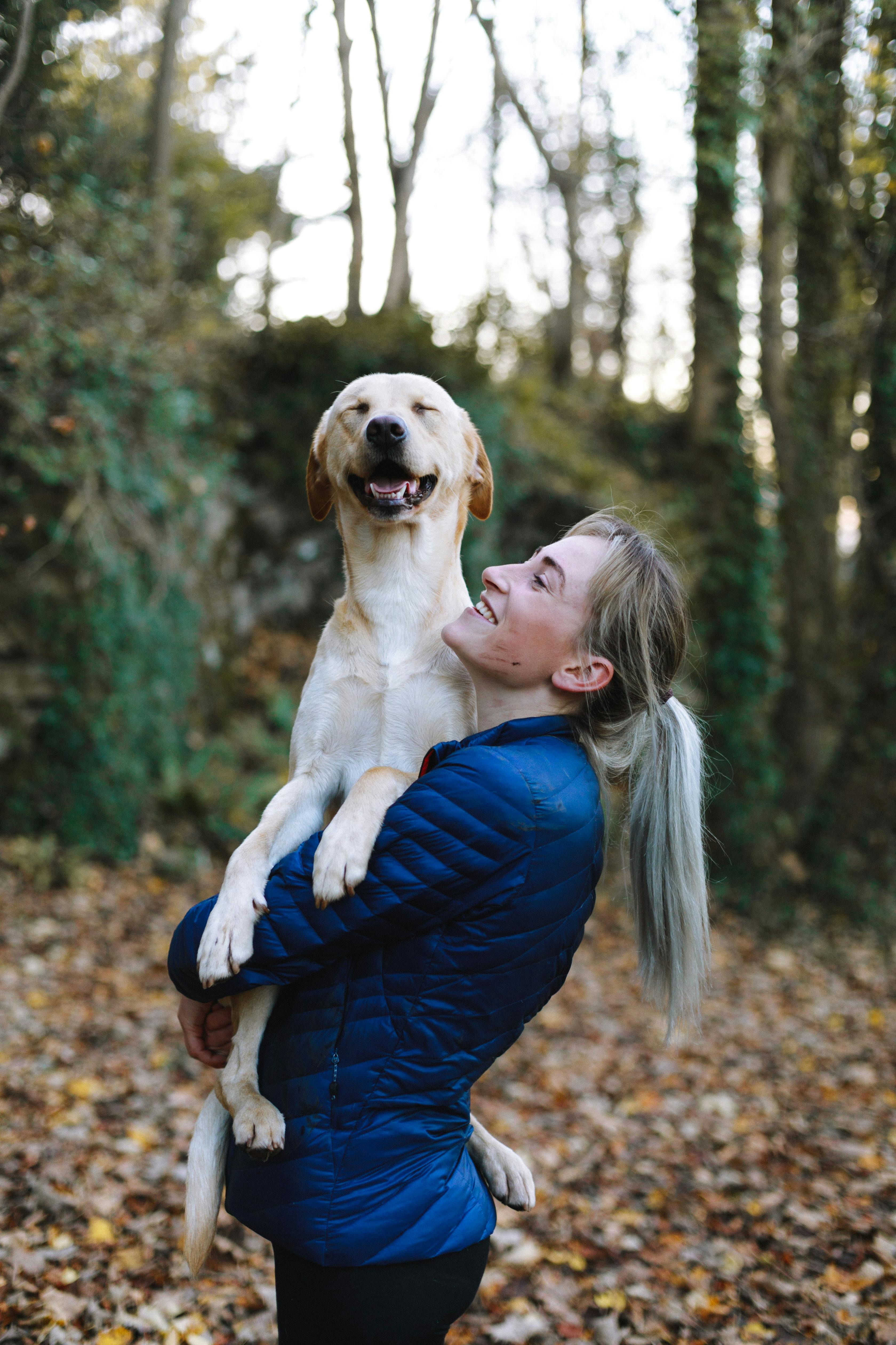 A white woman holds up her golden retriever. She is smiling up at the dog while the dog smiles at the camera.