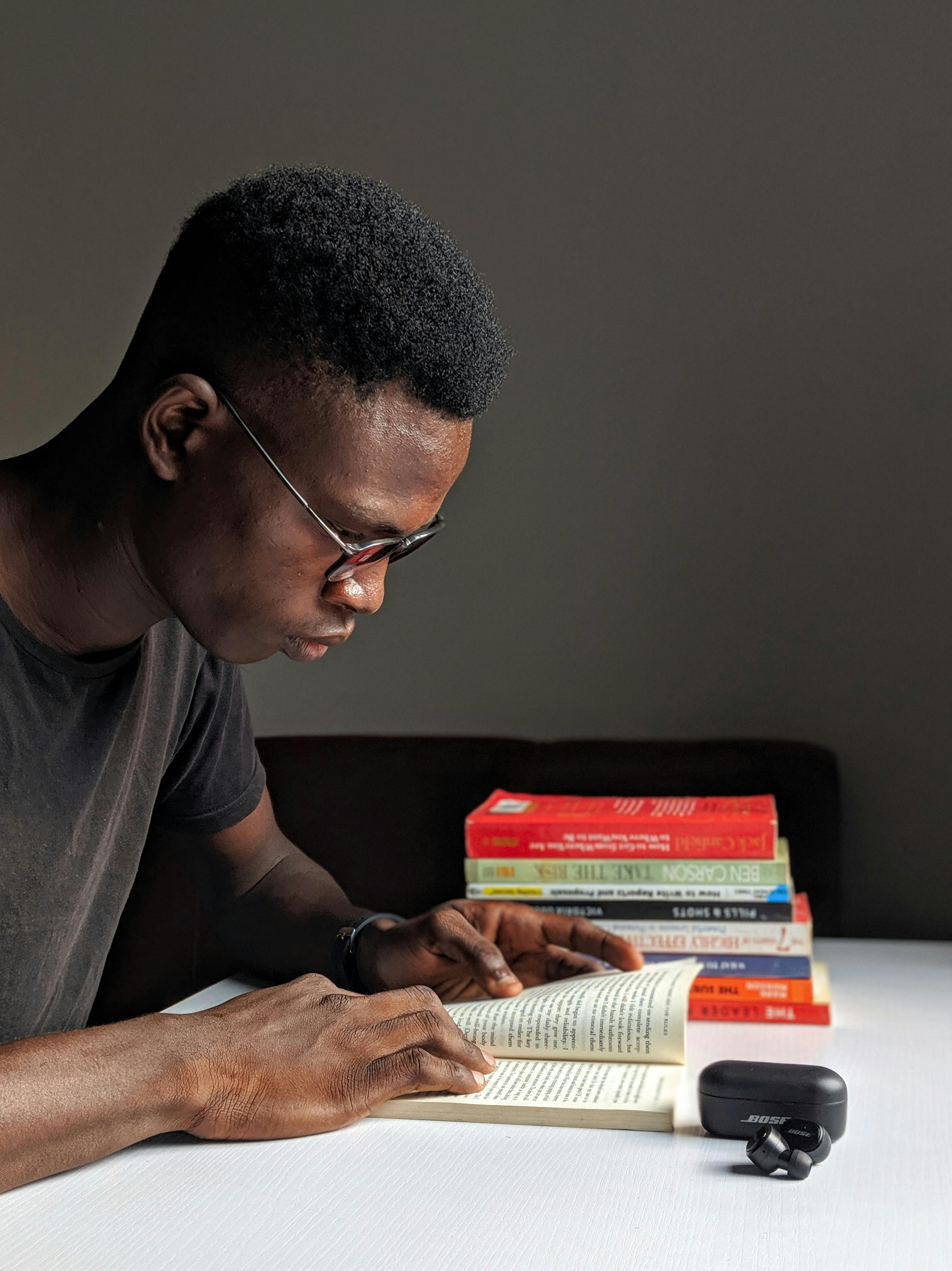 A young black man is reading books at a desk.