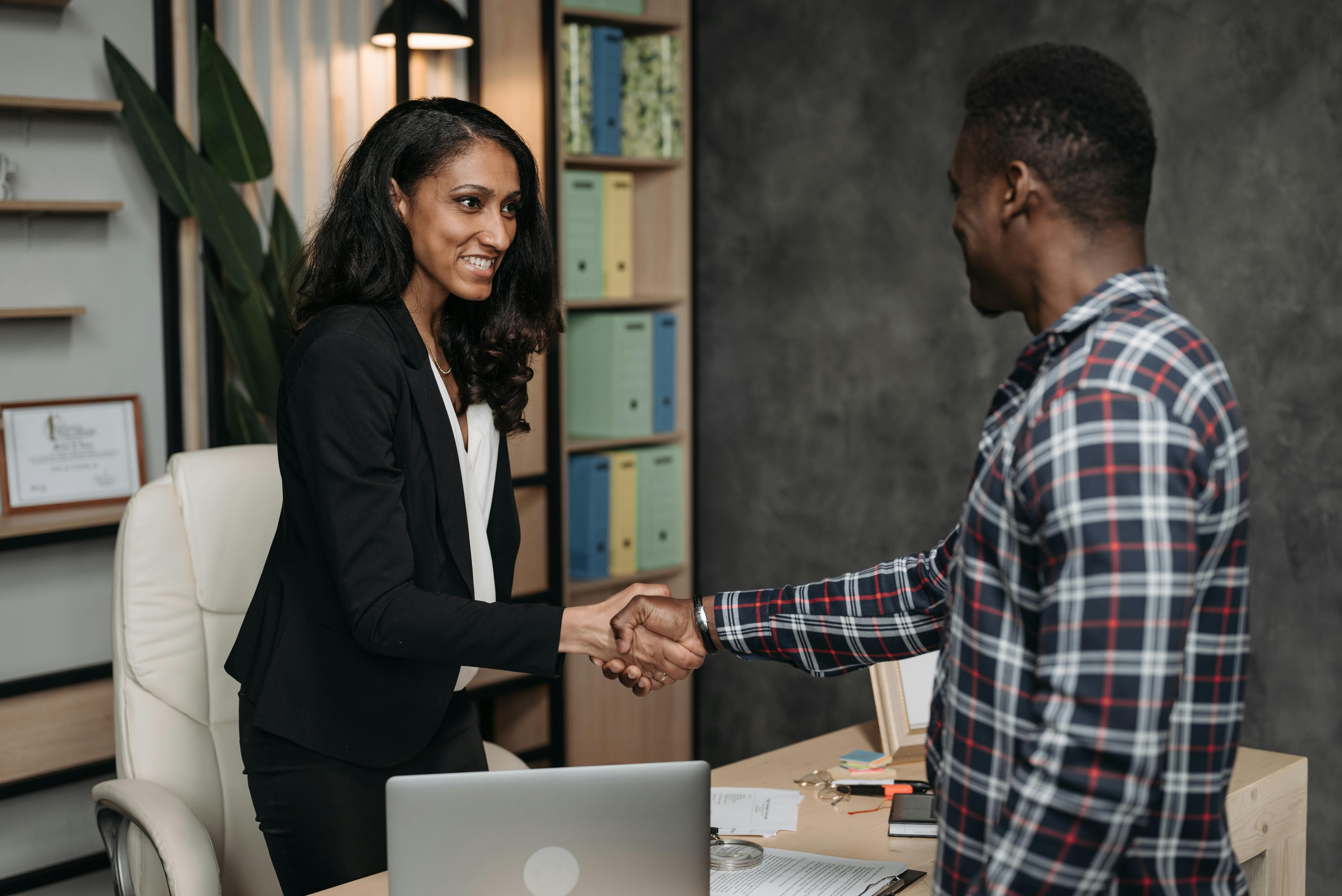 A black female lawyer stands behind a desk. She is shaking the hand of a black male client.