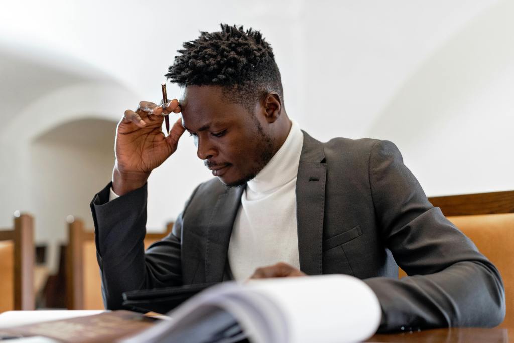A young black man sits at a desk in a suit. He is looking at his divorce papers with a somber expression.
