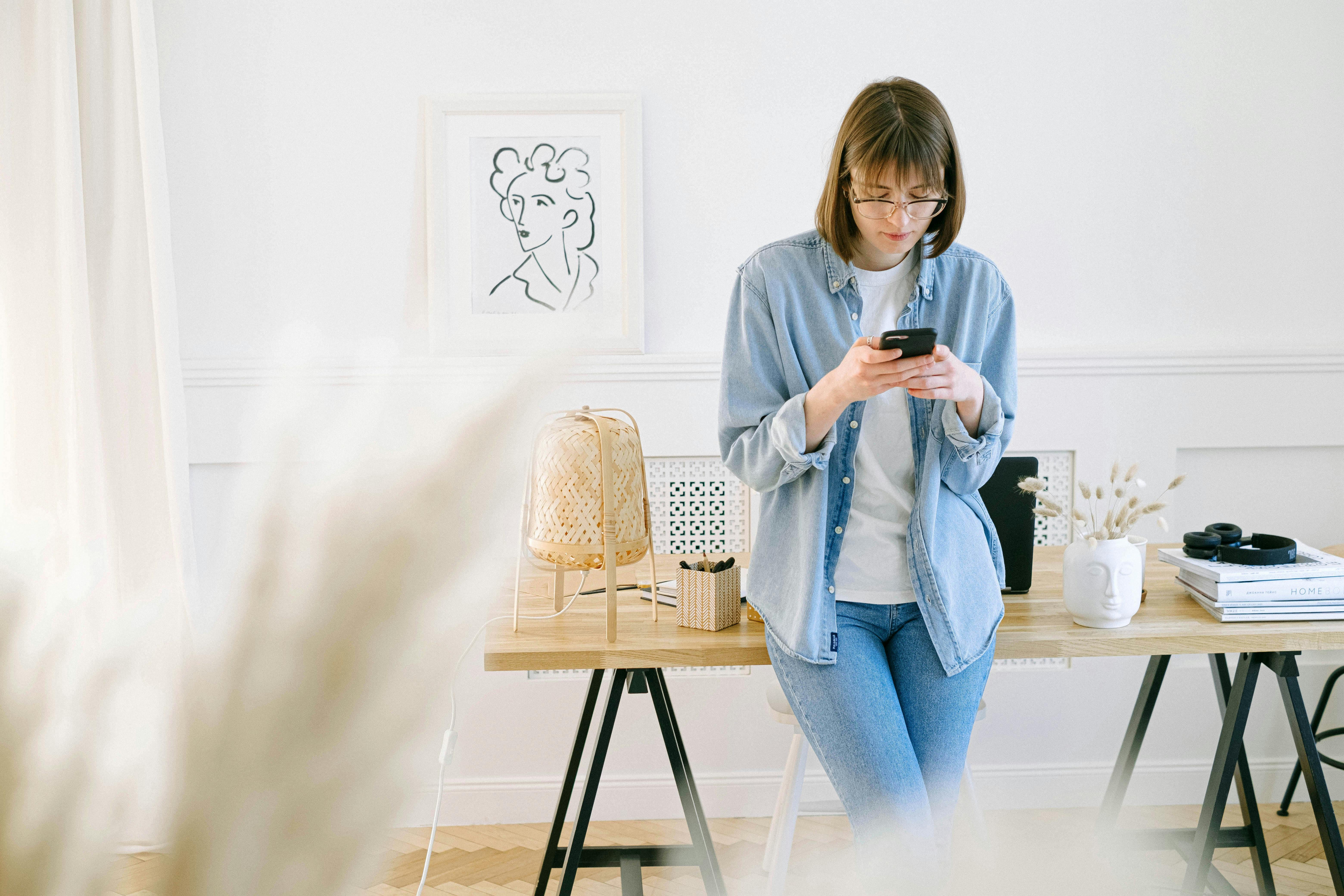A young woman leans against a table and is texting someone.