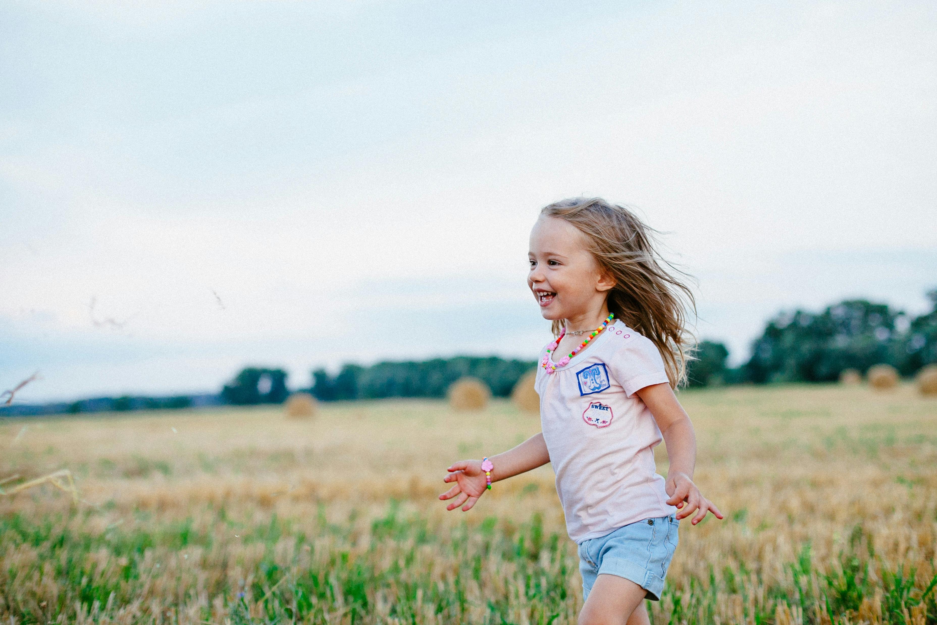 A white toddler is running through a field while smiling.
