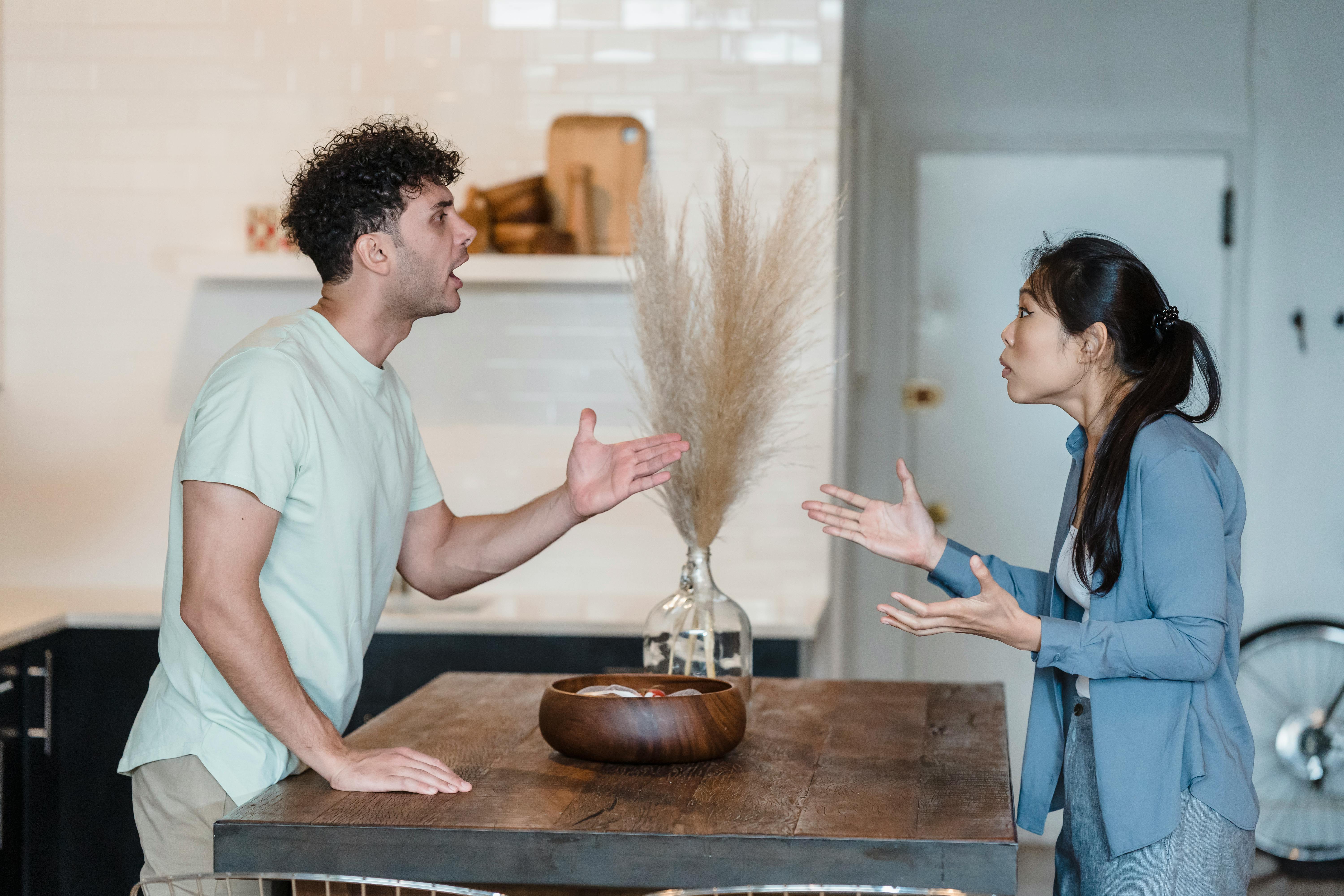 A BIPOC husband is arguing over a table with his female Asian partner.