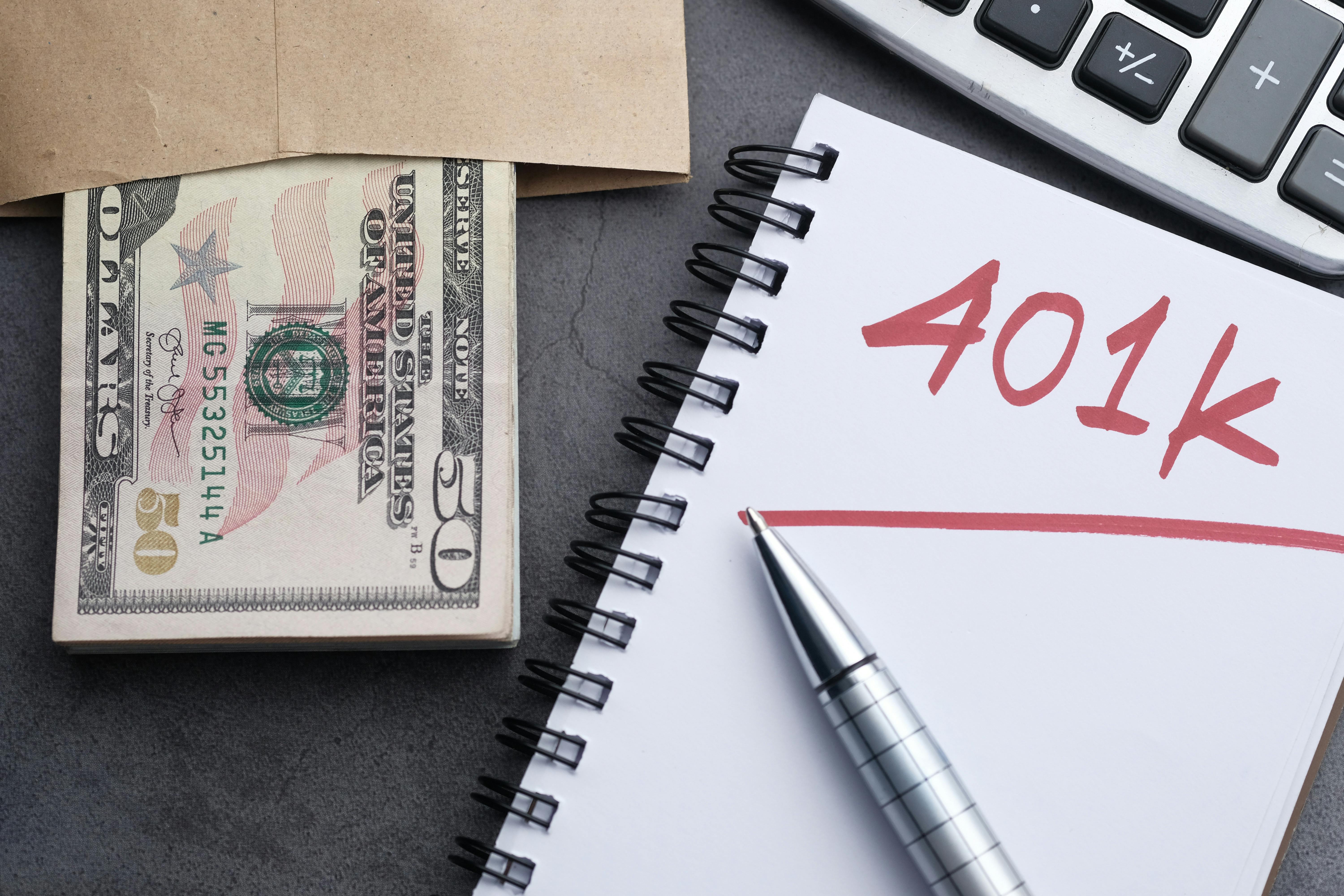Money, a calculator, and a notebook that has 401K written on it are on a table.