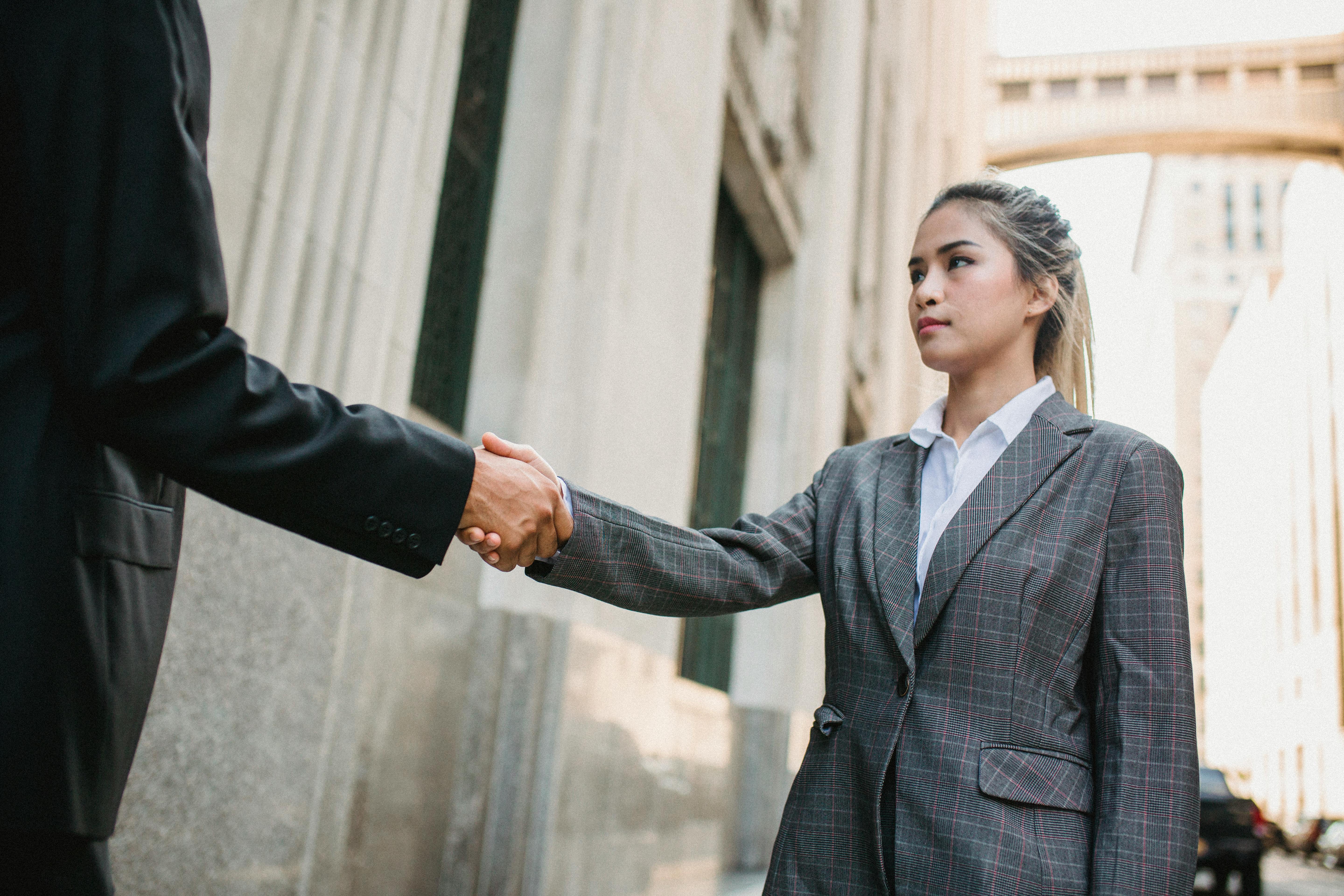 A young Asian woman is in a business suit outside of a courthouse. She is shaking the hand of her off-screen divorce attorney.