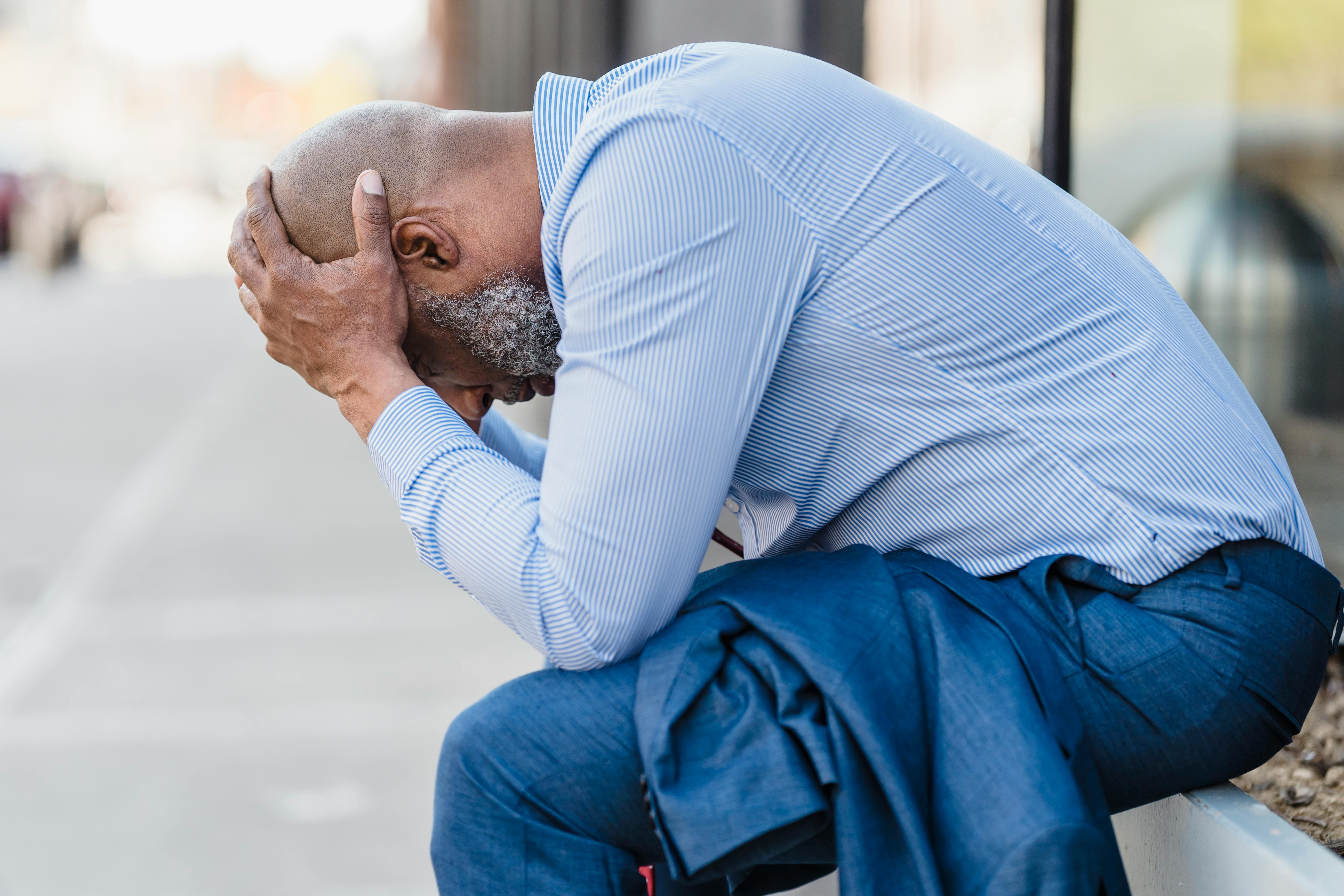 A middle-aged black man is sitting outside with his head resting in his hands as he contemplates his no-fault divorce.