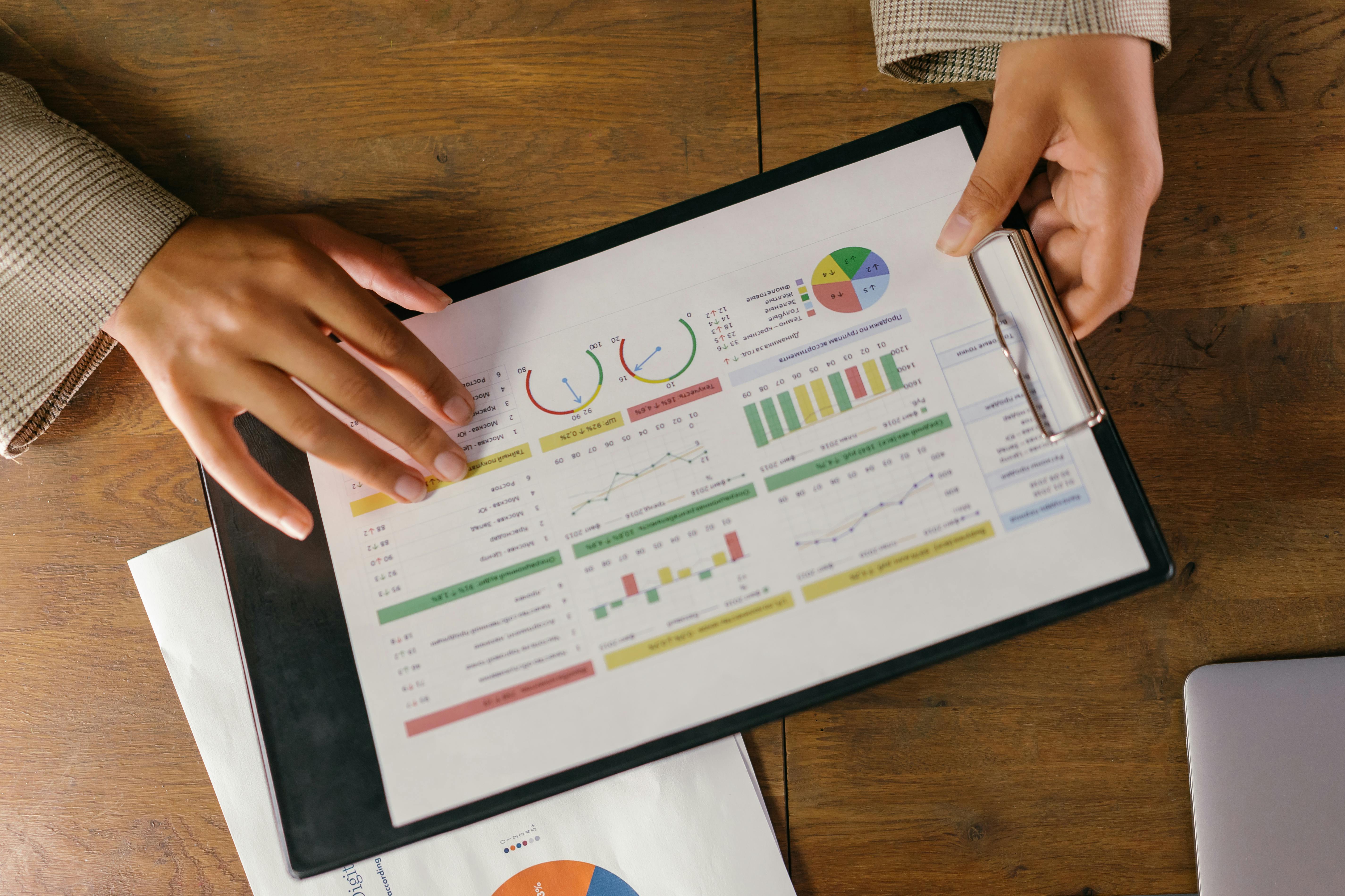 Two hands hold a clipboard. On the clipboard are charts, figures, and financial statistics.