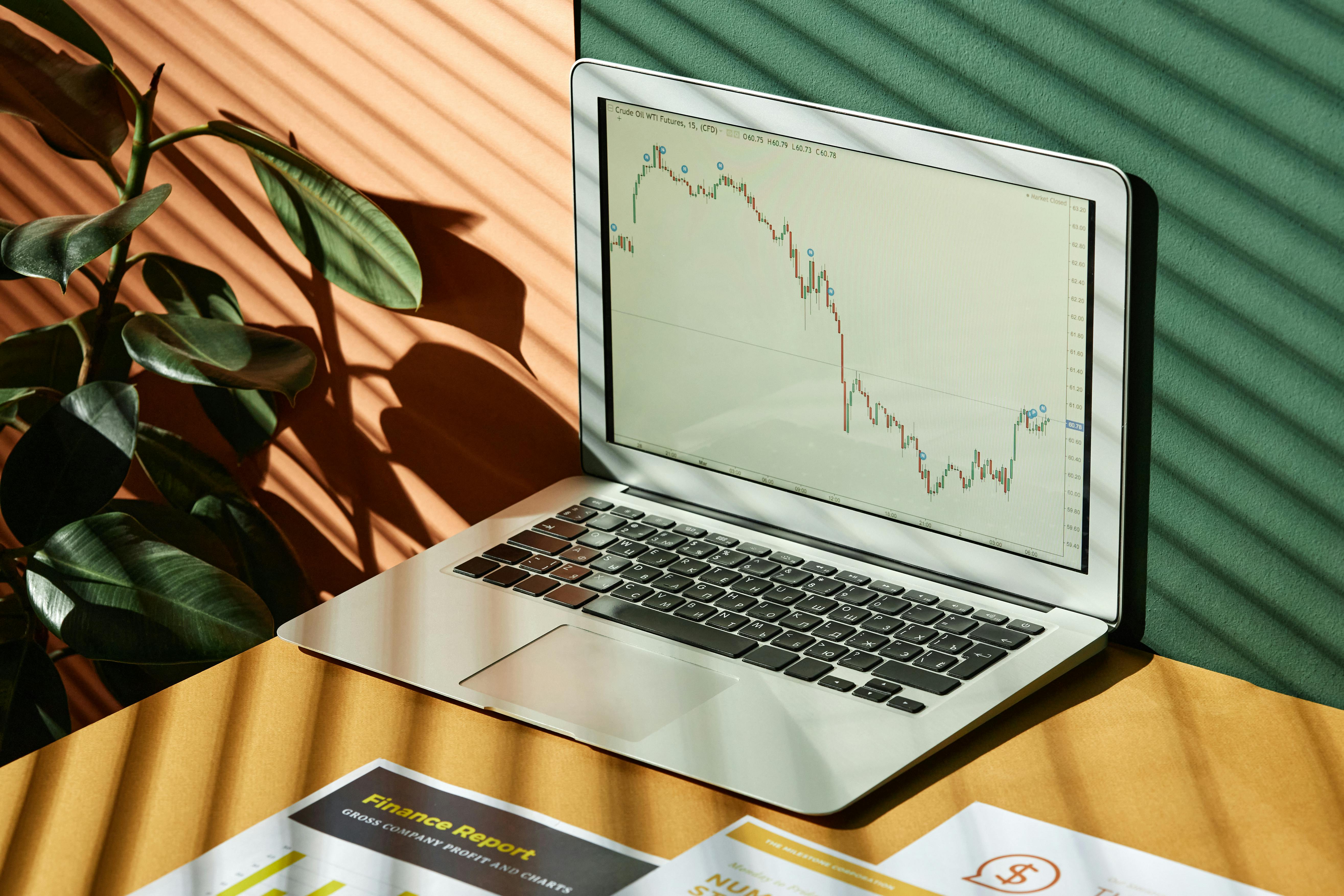 A laptop is on a desk. Open on the screen is a large graph showing financial losses with a slight gain at the end.