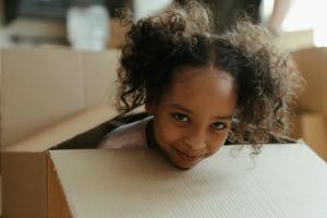 A young black girl is sitting in a moving box. Her family is relocating after divorce.