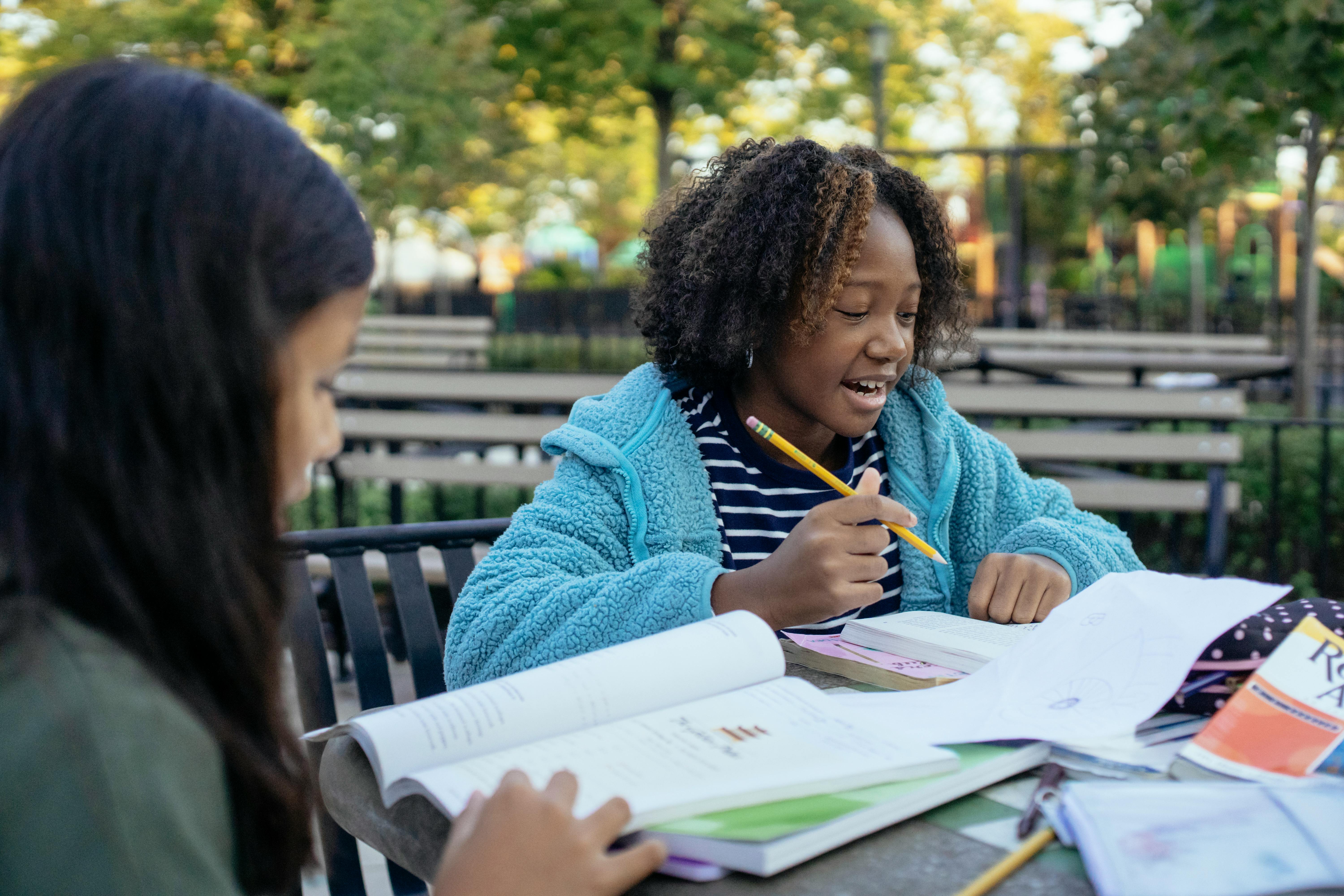 A young Asian girl sits with her young black friend at a table. They're working on homework together.