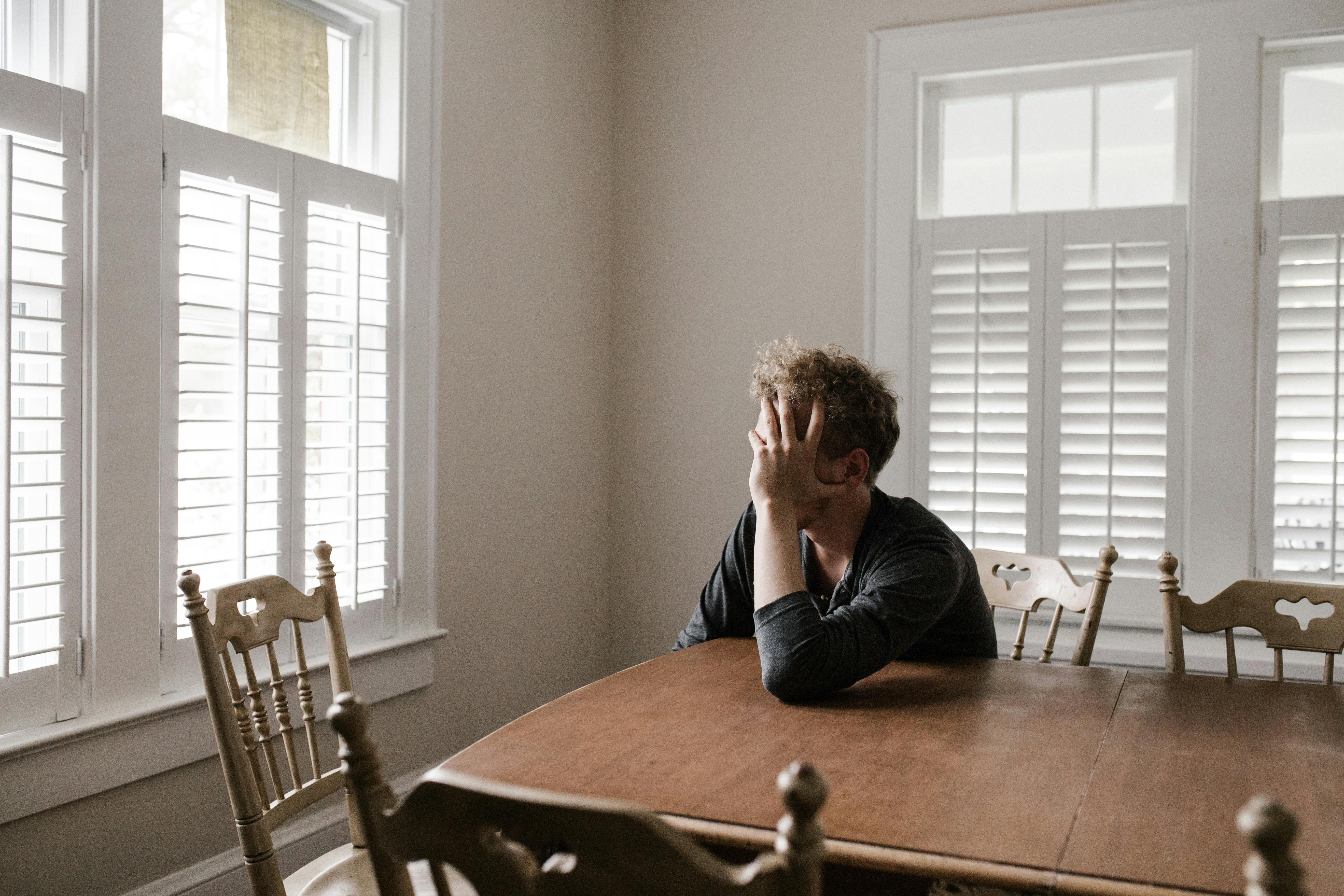 Young man with head in his hands, staring out the window as he struggles with a high conflict divorce