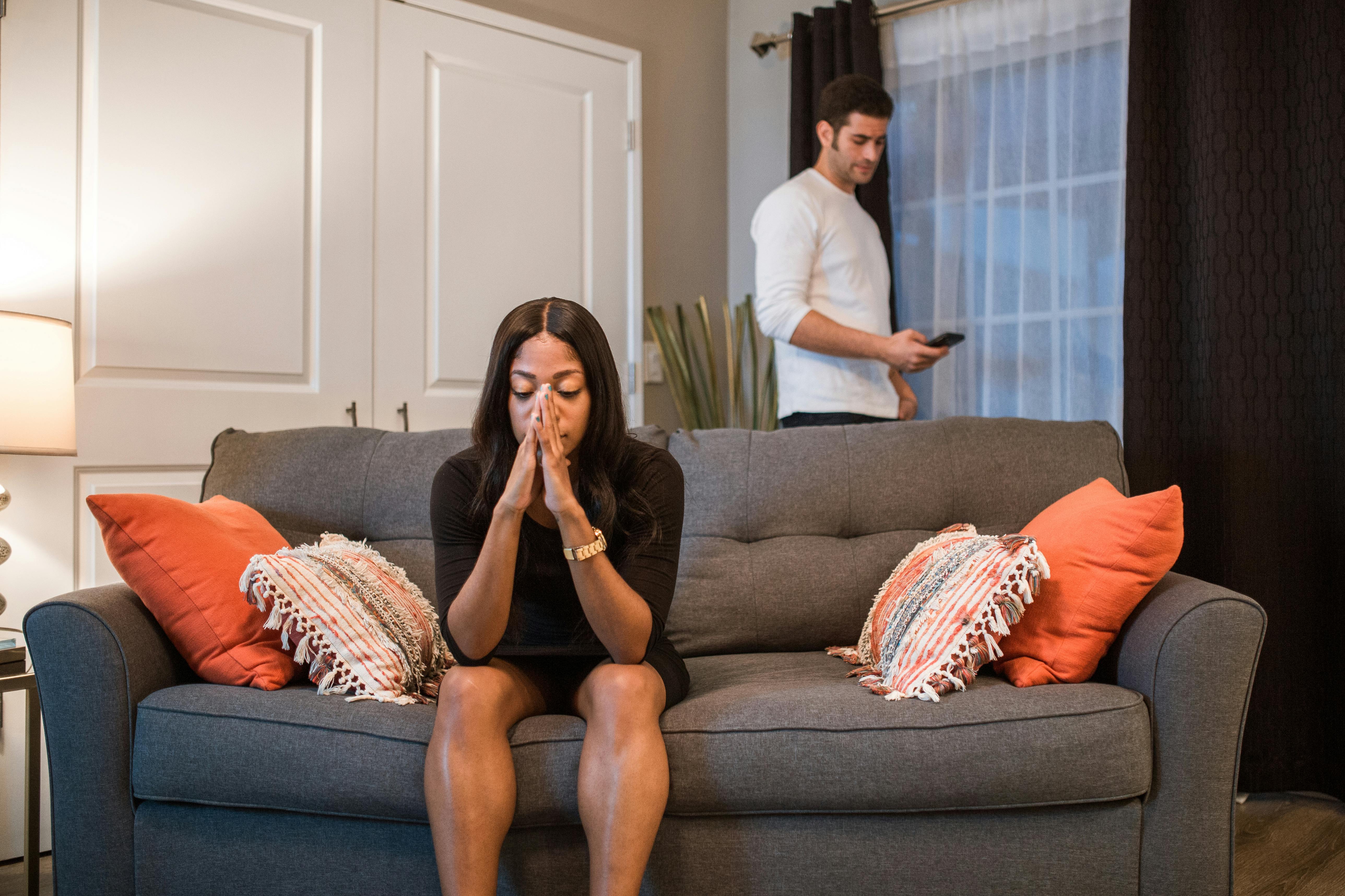Women sitting on the couch with head in her hands frustrated about her divorce. Man on his phone in the background.